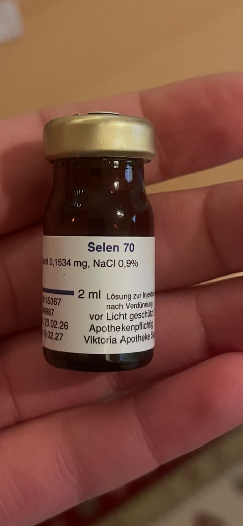 Small dark glass vial labeled Selen 70 held in hand, showing pharmaceutical label with dosage information and German text